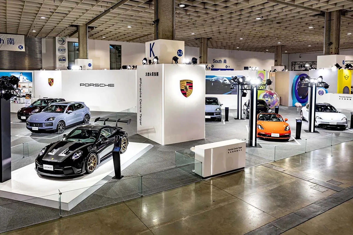 Premium automotive exhibition with vehicles on raised platforms, branded structures, and professional lighting
