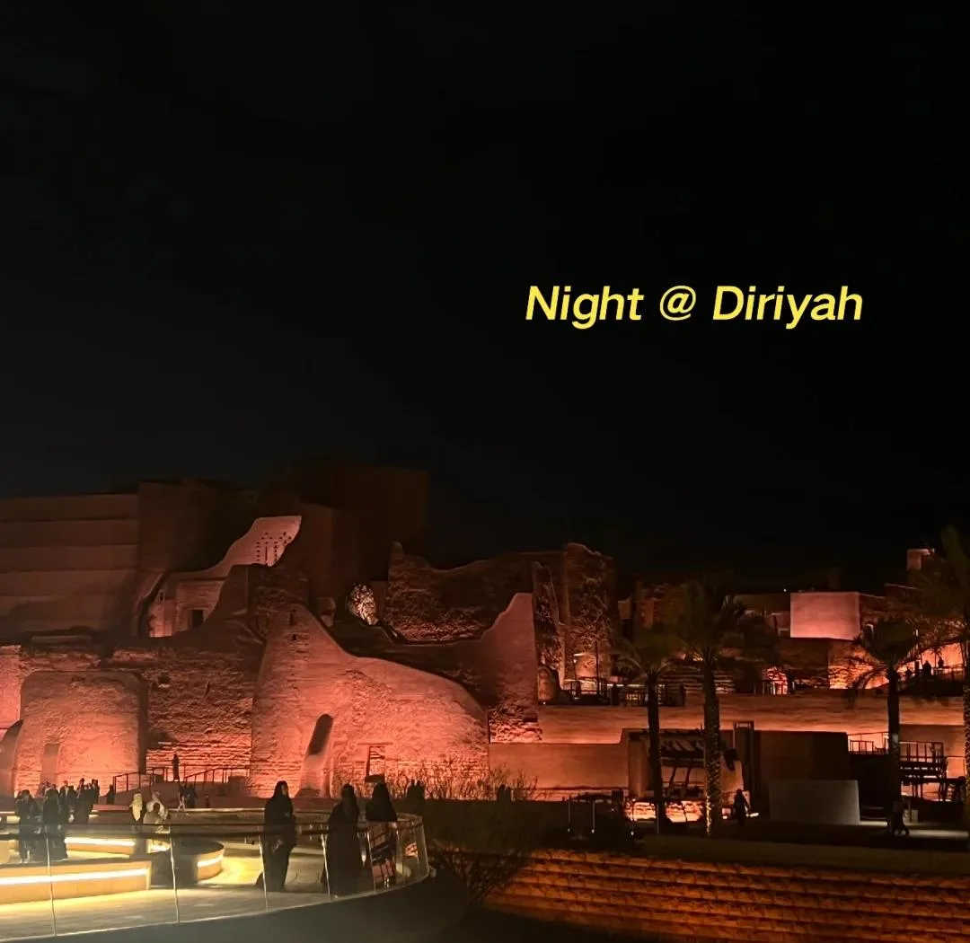 Diriyah At-Turaif UNESCO heritage site at night — warm-lit mud-brick architecture with palm trees and modern viewing platform