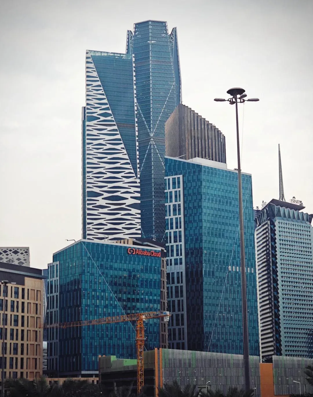 KAFD street-level view — modern glass skyscrapers with Alibaba Cloud building and geometric facades under overcast sky