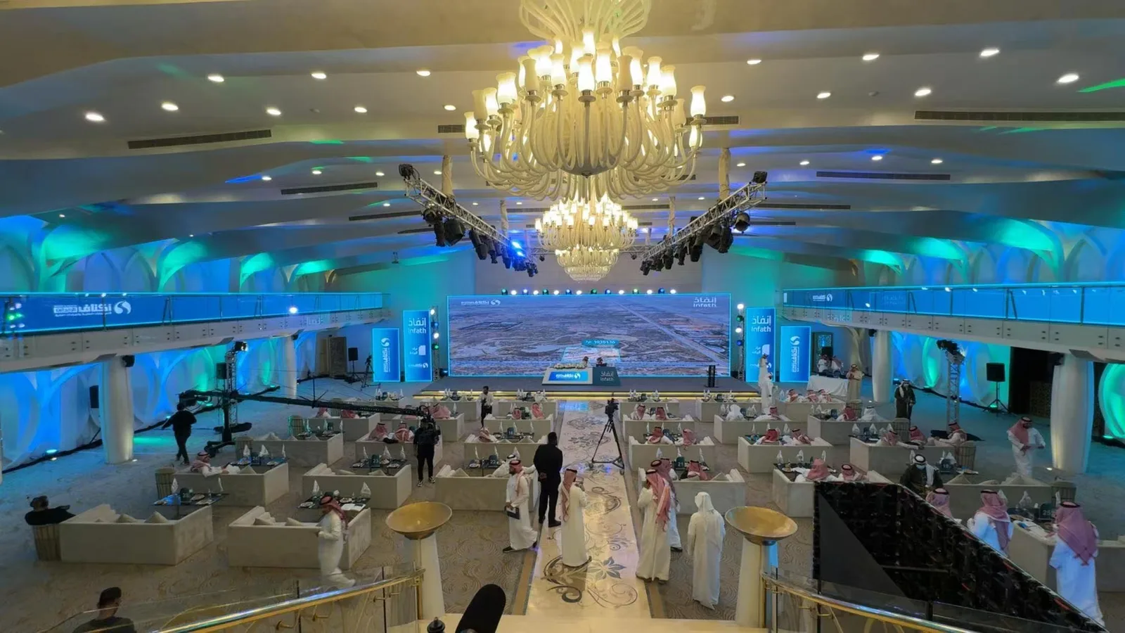 Elegant event hall fully staged with round dining tables, floral arrangements, chandeliers, and guests mingling